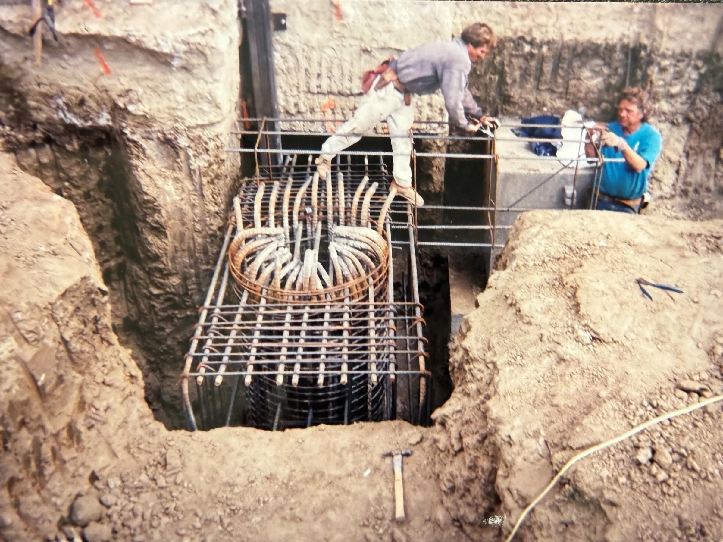 Workers placing rebar in a deep grade beam excavation tying into the Planet Pacific foundation